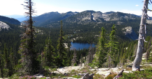 A scenic view of a mountain landscape with a serene lake surrounded by evergreen trees and rocky terrain.