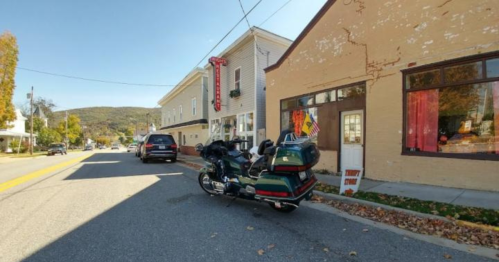 A motorcycle parked on a street beside a building with a red sign and colorful window displays.