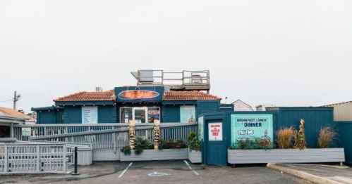 A blue restaurant with a sign saying "Open," featuring outdoor seating and a rooftop area.