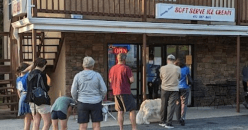 A line of people waiting outside a soft serve ice cream shop, with a dog near the entrance.