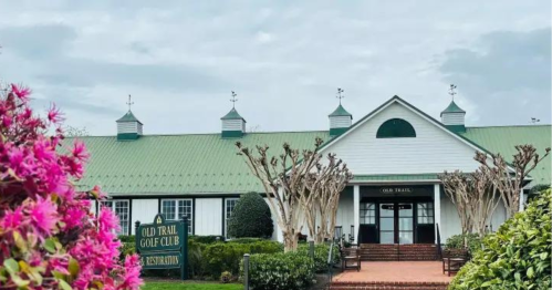 A charming golf club building with a green roof, surrounded by colorful flowers and well-maintained landscaping.