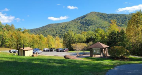 A scenic view of a parking area surrounded by trees and mountains under a clear blue sky.