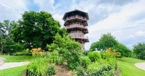 A tall wooden tower surrounded by lush greenery and colorful flowers under a cloudy sky.