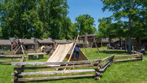 Reconstructed historic buildings in a grassy area surrounded by trees at Fort Boonesborough State Park in Kentucky on a sunny day