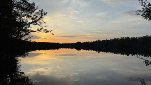 A fiery sunset above Atsion Lake in New Jersey, with the trees in dark silhouette in the distance.