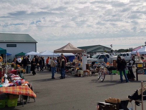 A bustling outdoor market with various stalls, people browsing, and tents under a cloudy sky.