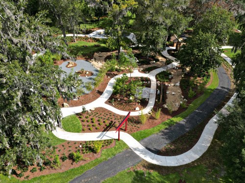 Aerial view of a landscaped park featuring winding paths, gardens, and greenery.