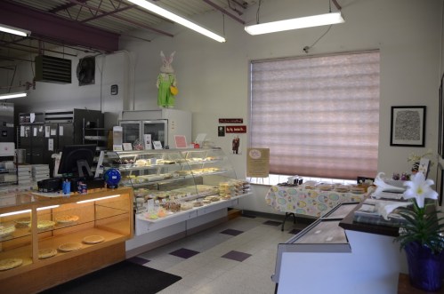 A cozy bakery interior with display cases of pastries, a cash register, and a large window with a bunny decoration.
