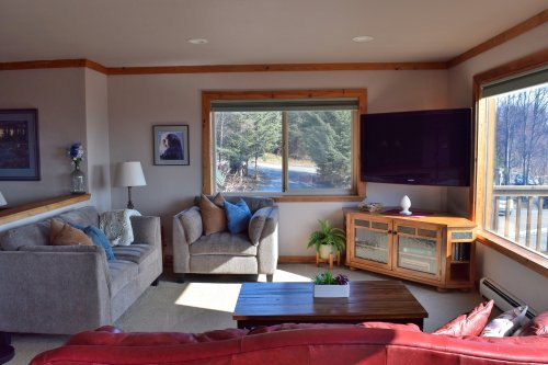 Cozy living room with a gray couch, armchair, wooden coffee table, and large windows overlooking a scenic view.