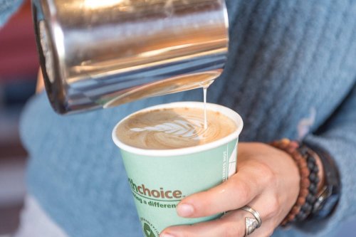 A person pours steamed milk into a coffee cup, creating a latte art design resembling a leaf.