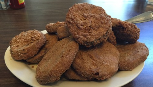 A plate piled high with golden-brown, fried doughnut-like treats, dusted with sugar.