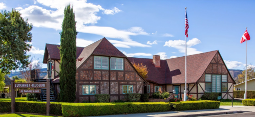 A charming museum building with a mix of architectural styles, featuring flags and landscaped greenery.