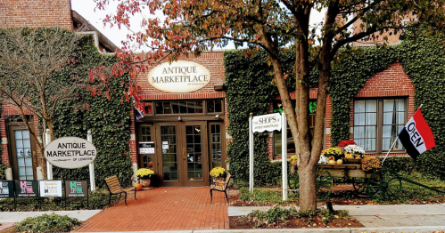A charming antique marketplace with ivy-covered brick walls, colorful flowers, and an "Open" sign outside.
