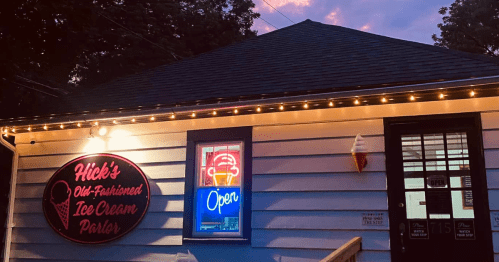 A charming ice cream parlor with a neon "Open" sign and decorative lights, set against a twilight sky.