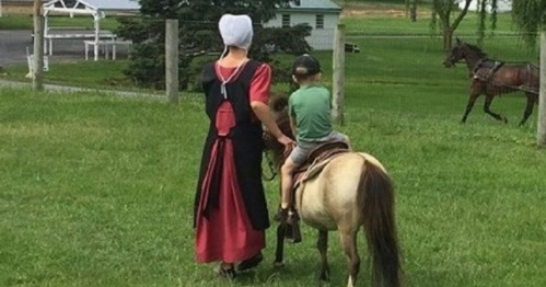 A child rides a small horse while an adult in traditional attire guides them in a grassy area.