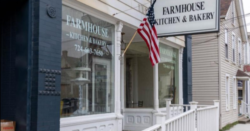 Exterior of Farmhouse Kitchen & Bakery, featuring a sign and an American flag, with a white porch and large windows.