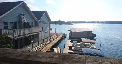 A serene lakeside view featuring a building, docks, and boats under a bright sky.