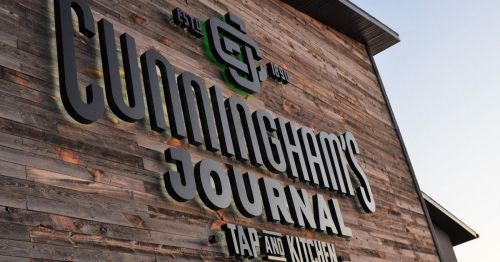 Sign for Cunningham's Journal Tap and Kitchen, featuring a wooden background and bold lettering.