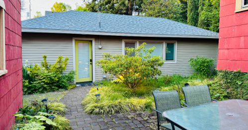 A cozy house with a yellow door surrounded by greenery and a patio set in a garden area.