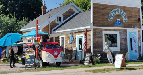 A charming shop with a vintage VW van outside, featuring outdoor seating and colorful umbrellas.
