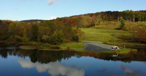 A serene landscape featuring a calm lake, lush greenery, and autumn-colored trees reflecting in the water.