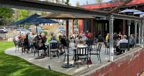 A lively outdoor dining area with people seated at tables under umbrellas, enjoying a sunny day.