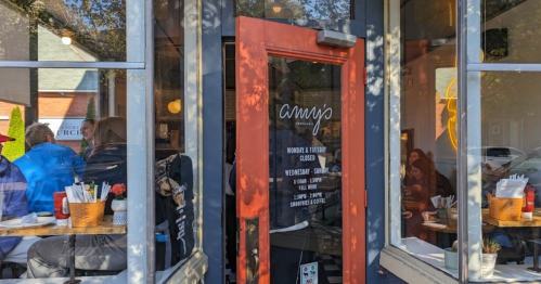 A cozy café entrance with a red door, featuring a menu board and patrons enjoying their meals inside.