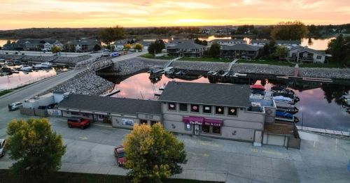 Aerial view of a marina at sunset, featuring a restaurant, boats, and residential buildings along the water.