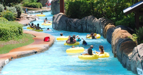 People floating on yellow inner tubes in a winding lazy river surrounded by greenery and rocks on a sunny day.