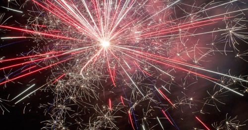 Colorful fireworks burst in the night sky, creating a dazzling display of red, white, and blue sparks.