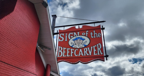 Sign for "Sign of the Beefcarver" featuring a cartoonish character, against a backdrop of cloudy skies.