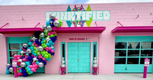 Colorful balloon arch at the entrance of a pink building with "FUNKITFIED" sign and teal doors.