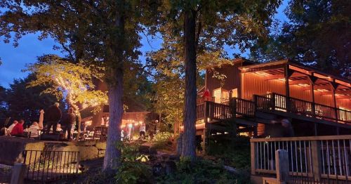 A cozy outdoor restaurant illuminated by warm lights, surrounded by trees and people enjoying the evening.