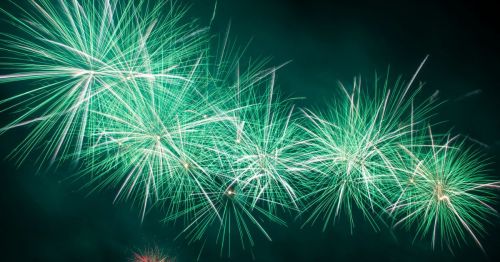 Bright green fireworks burst against a dark sky, creating a vibrant display of light and energy.
