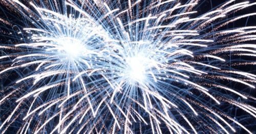 Bright white fireworks burst against a dark sky, creating a dazzling display of light and sparks.