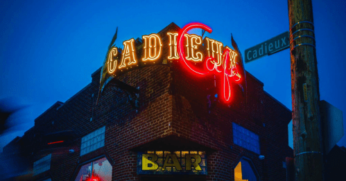 Neon sign for "Cadieux" bar at dusk, with a street sign for Cadieux Street visible.
