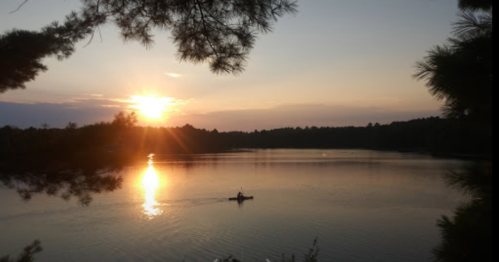 A serene sunset over a calm lake, with a lone kayaker paddling in the golden light.