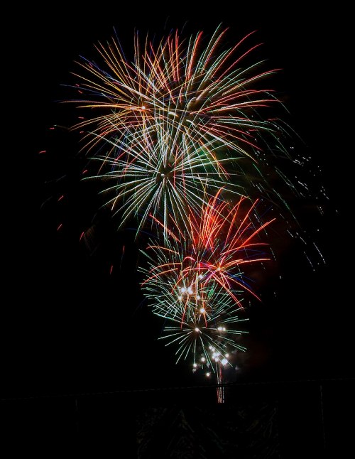 Colorful fireworks burst in the night sky, creating a vibrant display of red, green, and blue lights.