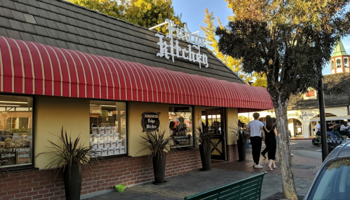 A storefront with a red awning and "Food Kitchen" sign, featuring people walking by and trees in the background.