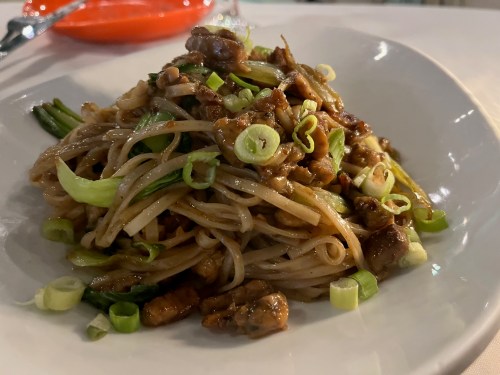 A plate of stir-fried noodles topped with chopped green onions and pieces of meat.