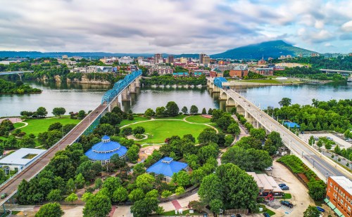 Aerial view of a city with bridges over a river, green parks, and buildings against a cloudy sky.