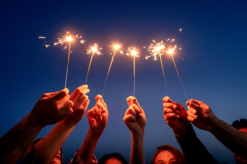 A group of hands holding sparklers against a twilight sky, creating a festive and joyful atmosphere.