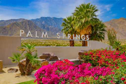 Sign reading "Palm Springs" surrounded by vibrant flowers and palm trees, with mountains in the background.