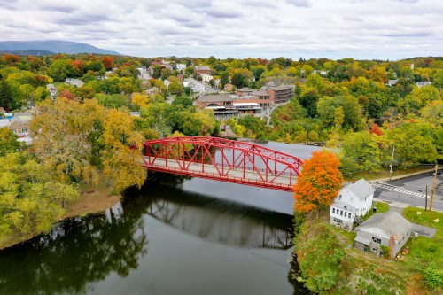 A red bridge spans a river, surrounded by colorful autumn trees and a small town in the background.
