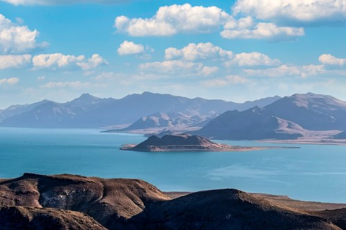 A serene landscape featuring a calm blue lake surrounded by mountains and a partly cloudy sky.