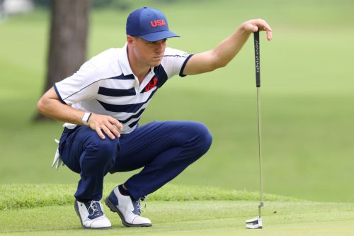 A golfer in a USA shirt crouches down, focusing intently on his putt on a green golf course.