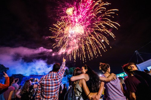 A group of people watch colorful fireworks explode in the night sky, celebrating together at an outdoor event.