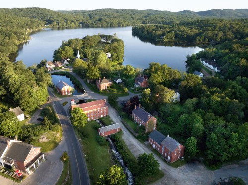 Aerial view of a serene lakeside village surrounded by lush greenery and rolling hills.