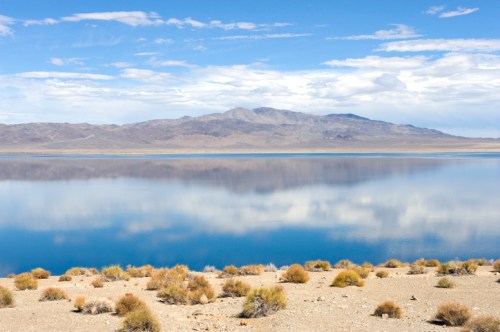 A serene landscape featuring a calm lake reflecting mountains under a blue sky with scattered clouds.