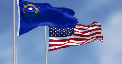 Nevada state flag and the United States flag waving against a blue sky.
